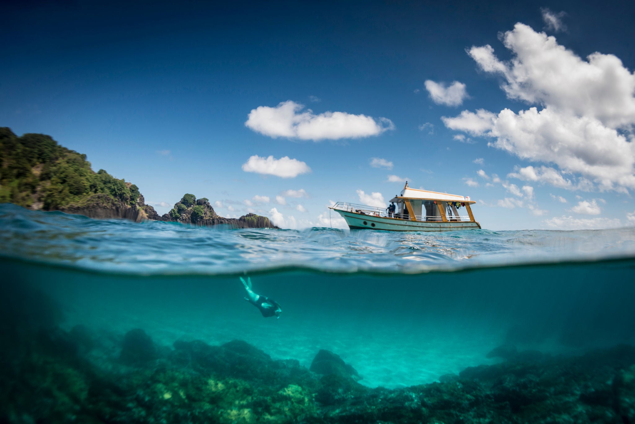 Small boat in the ocean with a person swimming to the bottom