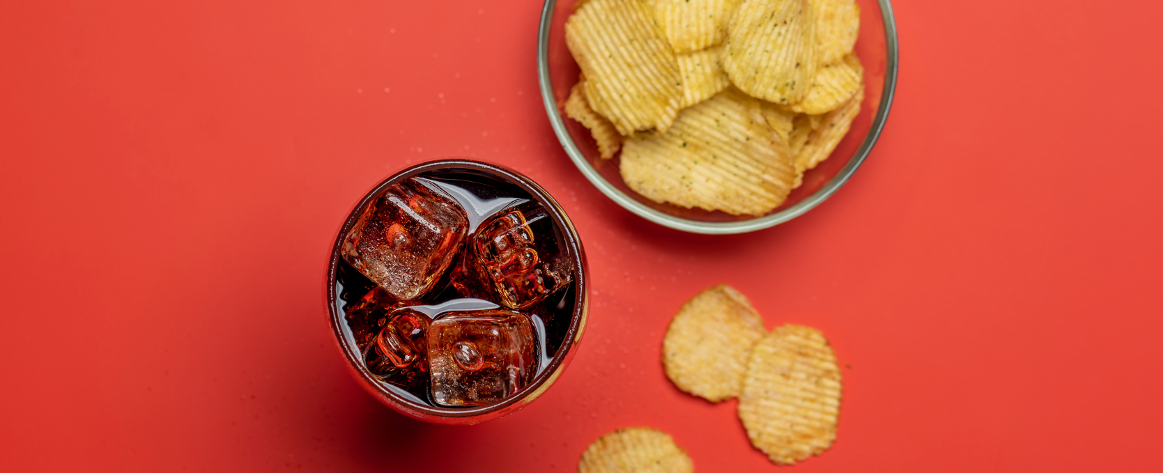 Bowl of crisps and a iced glass of a fizzy drink on a red background. 
