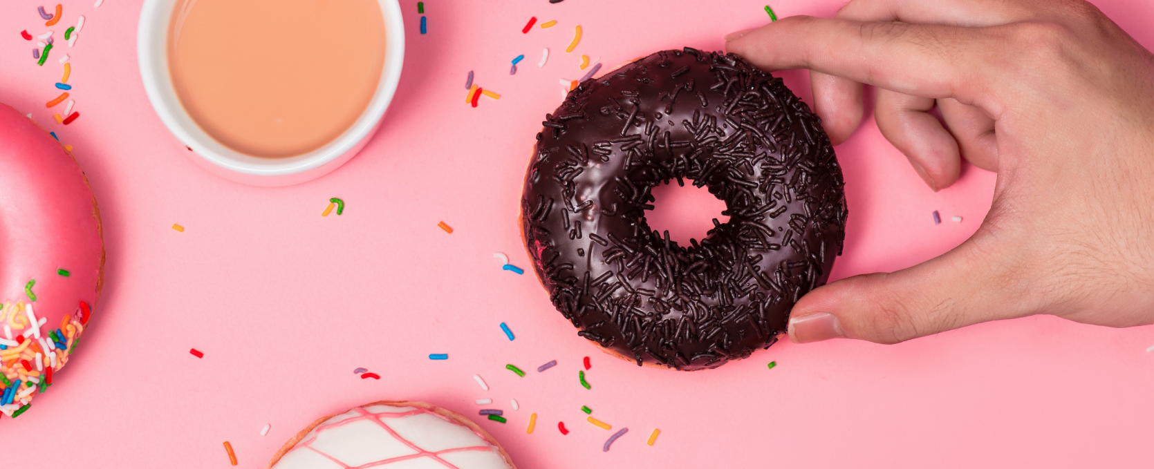 hand holding doughnuts with more doughnuts and a cup of tea against a pink background